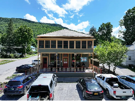 Historic two story building with porches on both levels, teal clapboard siding and restaurant on first floor. 