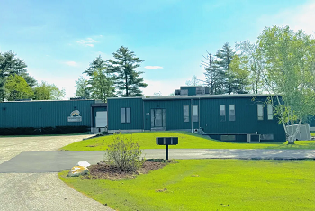 Slate gray industrial building set on a meadow with trees behind.