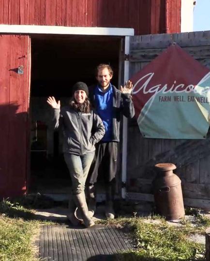 Agricola Farm owners standing in front of a barn door waving