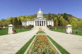 A view of the Vermont State House front with spring flowers in front and greening trees behind