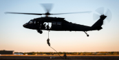 Silhouette of a helicopter at sunset with a soldier rappelling below