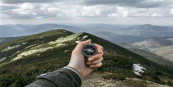 A photo of a hand holding a compass in front of a mountain range view