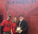 Fred, Tamara & Joey stand in front of a red wall painted with a Vermont map