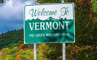 A "Welcome to Vermont" road sign, with fall foliage in the background.