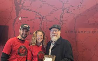 Fred, Tamara & Joey stand in front of a red wall painted with a Vermont map